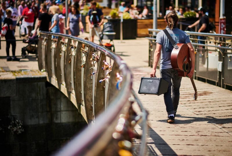 Guitarist walking along a bridge carrying their guitar and amplifier outdoor music scene at a popular Dublin location.