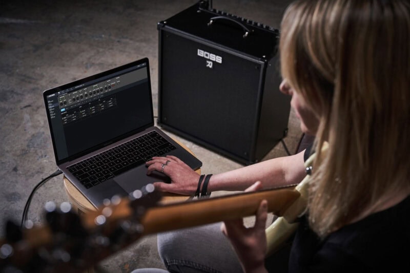Apple MacBook displaying music production software with a guitar in the foreground and a Black BOSS amplifier in the background.