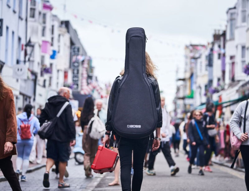 Guitar gig bag on woman’s back in busy street scene, colourful shops and pedestrians, music store visit, Dublin, Ireland.