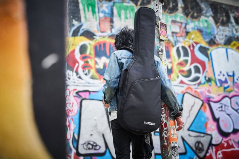 Black guitar case on a person's back in front of vibrant graffiti wall in Swords, Dublin.