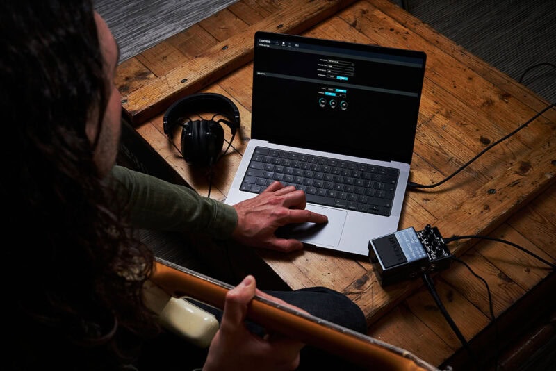 High-tech music studio setup with a musician using a MacBook, audio interface, headphones, and electric guitar for music production or practice.