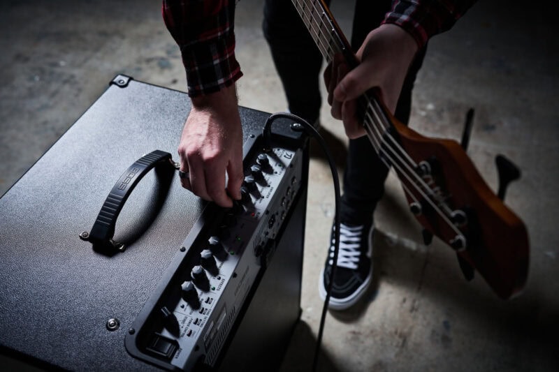 Electric bass guitar and amplifier being adjusted by a musician.