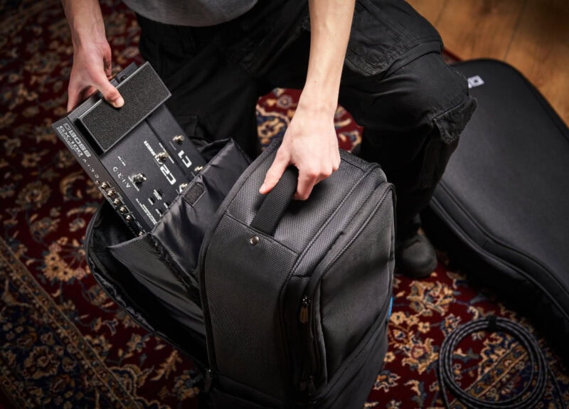 An individual packing a guitar effects pedal and cables into a black gig bag on a decorative red carpet in a music shop.