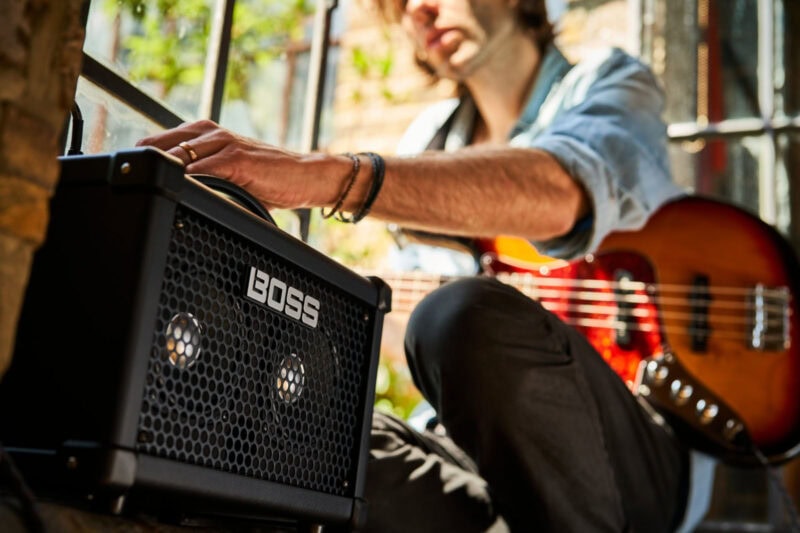 Bright outdoor scene with a man adjusting a BOSS guitar amplifier, while holding an acoustic guitar, in the sunlit interior of a musical instrument shop in Swords, Dublin.