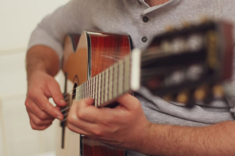 Hand strumming an acoustic guitar, focusing on fingers and fretboard, in a music shop setting.