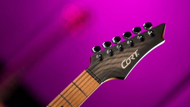 Guitar headstock with tuning pegs against a vibrant purple background.