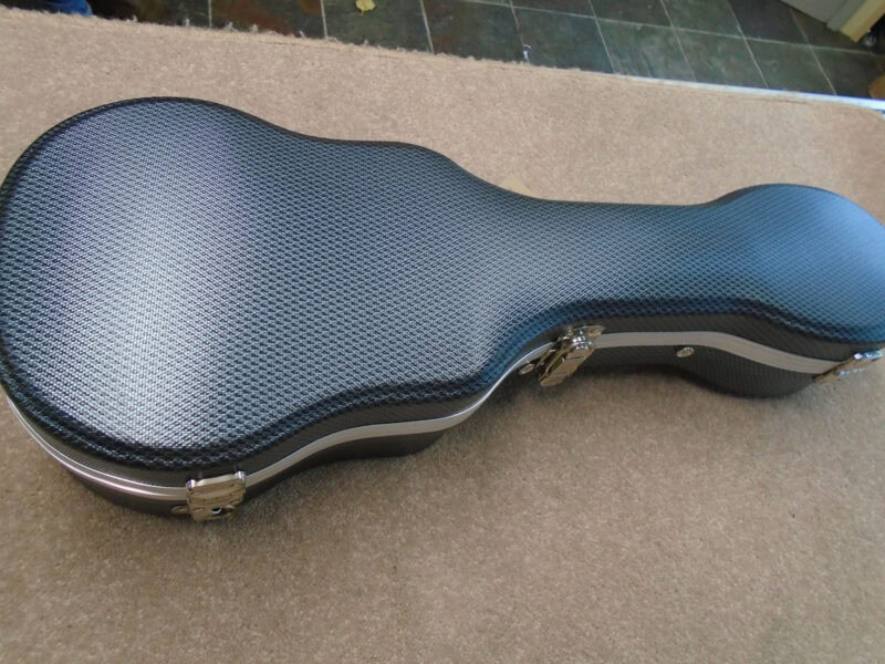 A sleek, black carbon fibre guitar case with silver hardware, designed to protect and carry an acoustic guitar securely.