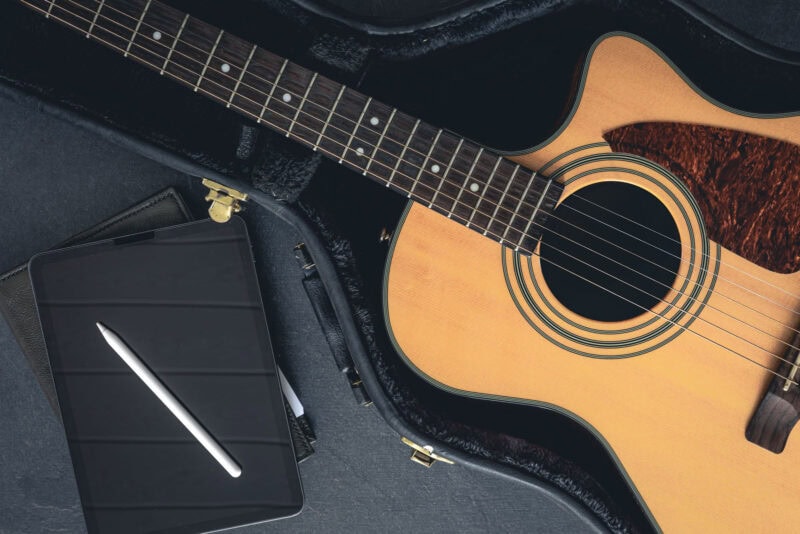Guitar in an open case alongside a digital tablet with a stylus inside a music store.